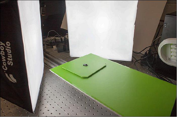 Figure 11: The green screen background, diffuse lighting, and turntable are shown in the image. The diffuse lighting is used to eliminate shadows that interfere with object detection in images. The green screen also improves object detection against the background. The object rests on a turntable that rotates incrementally through one full rotation during imaging (image credit: University of Florida, NASA)
