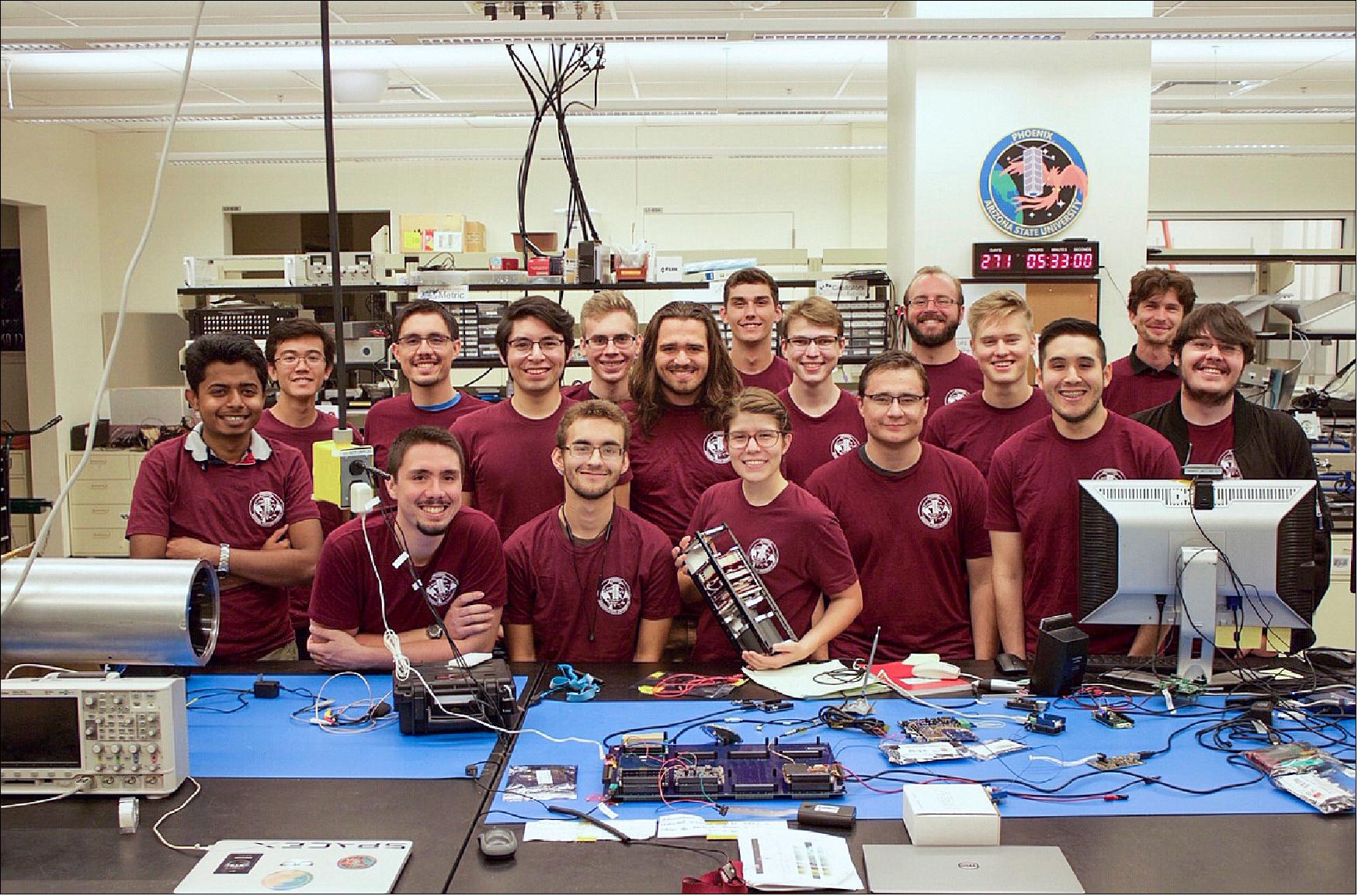 Figure 1: Members of the Phoenix student engineering team gather in the lab, with team lead Sarah Rogers holding a 3D test model of the Phoenix CubeSat. Electronic components on the bench are part of the development hardware (image credit: Craig Knoblauch/Arizona State University)