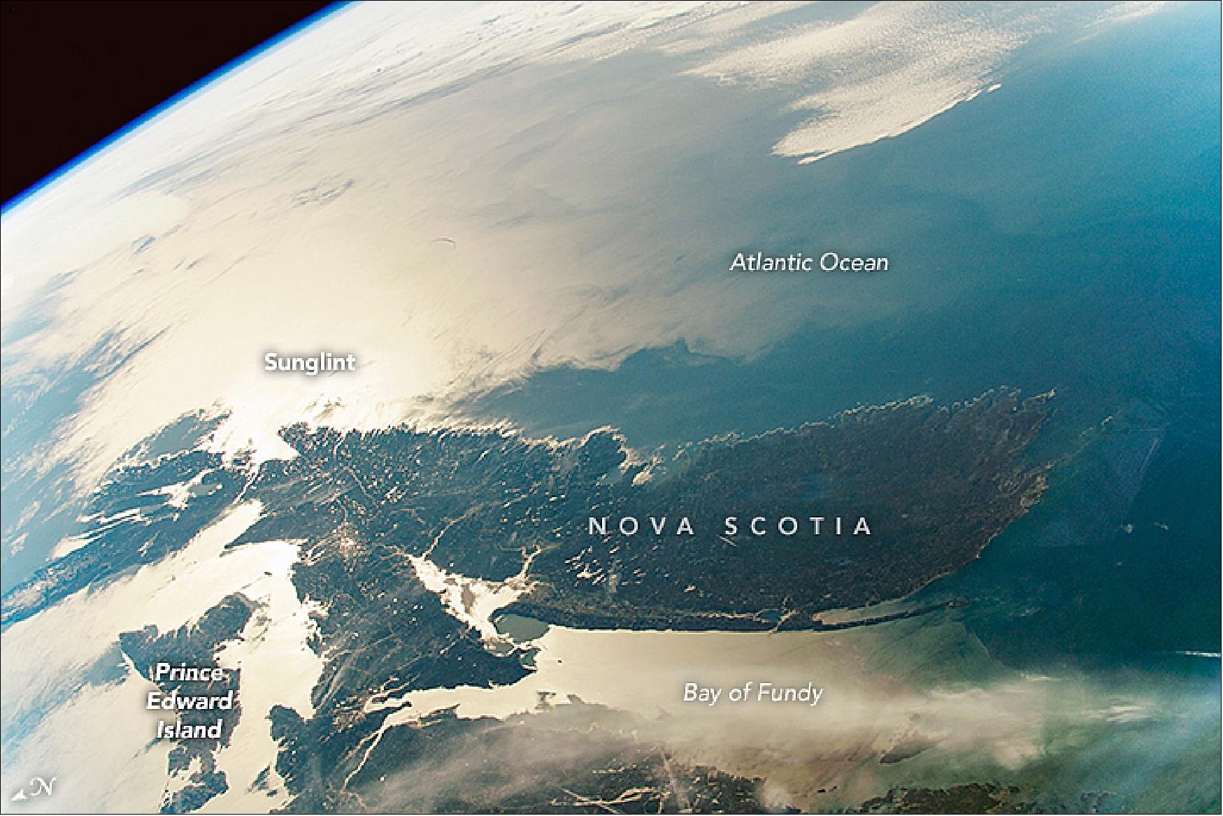 Figure 71: This photograph, observed on 7 May 2019, shows Nova Scotia to the east of the space station, contrasted against the brilliance of the Sun reflecting off of the Atlantic Ocean. “Sunglint” images like this can highlight fine coastline details: Nova Scotia’s shoreline, northern arms of the Bay of Fundy, and the outline of Prince Edward Island (image credit: Astronaut photographs ISS059-E-59135 and ISS059-E-52689 were acquired on 7 May 2019, with a Nikon D5 digital camera using 50 mm and 35 mm lenses (respectively) and are provided by the ISS Crew Earth Observations Facility and the Earth Science and Remote Sensing Unit, Johnson Space Center. The images were taken by a member of the Expedition 59 crew. Caption by M. Justin Wilkinson and Susan Runco)