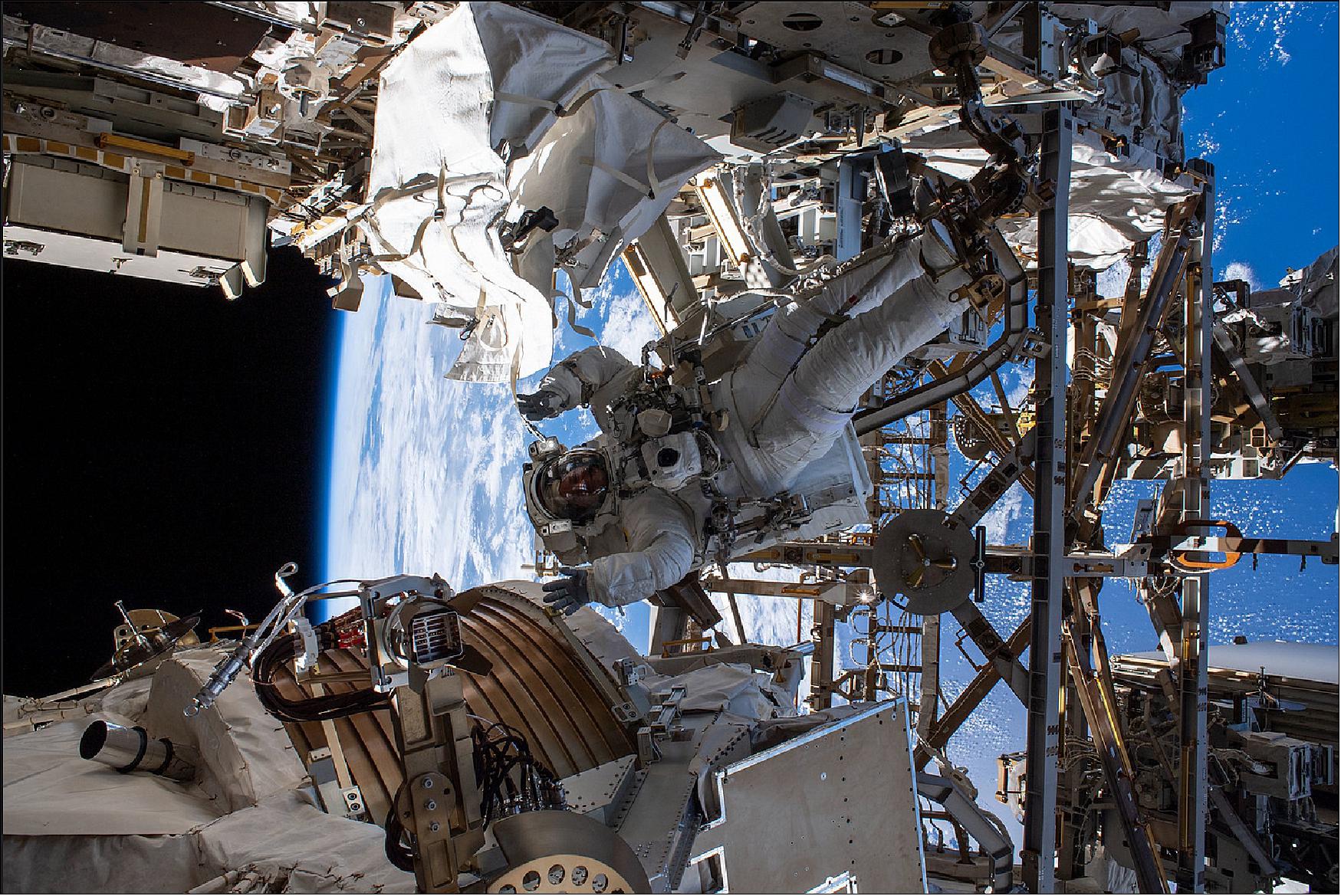 Figure 21: NASA astronaut Andrew Morgan waves as he is photographed (Nov. 15, 2019) seemingly camouflaged among the Alpha Magnetic Spectrometer (lower left) and other International Space Station hardware during the first spacewalk to repair the cosmic particle detector (image credit: NASA) 16)