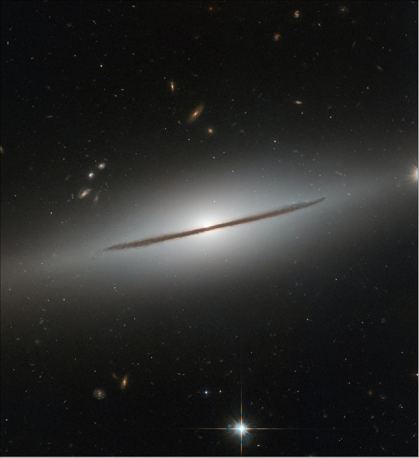 Figure 38: A handful of other galaxies can be seen lurking in the background, scattered around the narrow stripe of NGC 1032. Many are oriented face-on or at tilted angles, showing off their glamorous spiral arms and bright cores. Such orientations provide a wealth of detail about the arms and their nuclei, but fully understanding a galaxy’s three-dimensional structure also requires an edge-on view. This gives astronomers an overall idea of how stars are distributed throughout the galaxy and allows them to measure the “height” of the disc and the bright star-studded core (image credit: ESA/Hubble & NASA, CC BY 4.0)