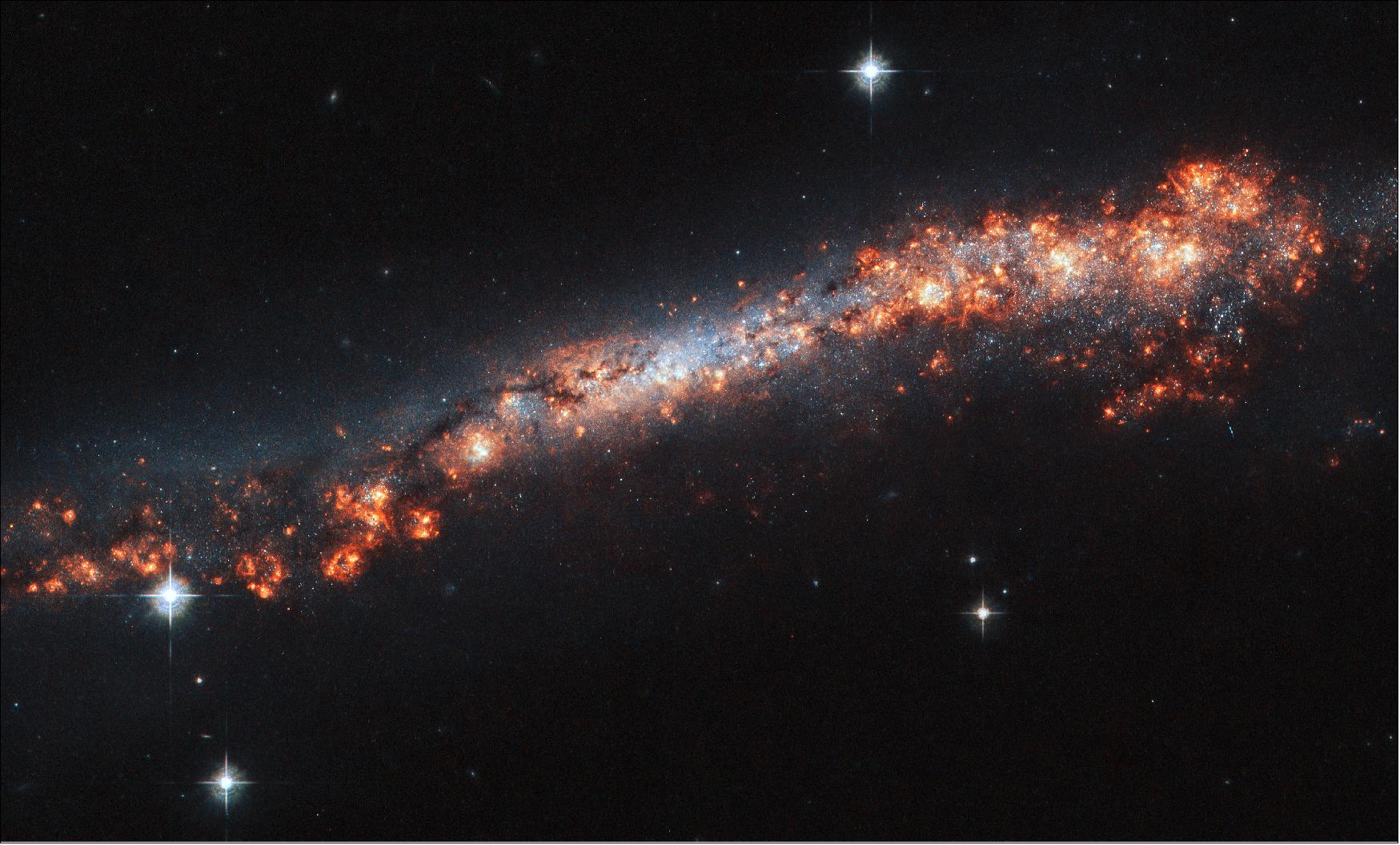 Figure 33: It turns out that we see this galaxy, named NGC 3432, orientated directly edge-on to us from our vantage point here on Earth. The galaxy’s spiral arms and bright core are hidden, and we instead see the thin strip of its very outer reaches. Dark bands of cosmic dust, patches of varying brightness, and pink regions of star formation help with making out the true shape of NGC 3432 — but it’s still somewhat of a challenge! Because observatories such as the NASA/ESA Hubble Space Telescope have seen spiral galaxies at every kind of orientation, astronomers can tell when we happen to have caught one from the side (image credit: ESA/Hubble & NASA, A. Filippenko, R. Jansen; CC BY 4.0)