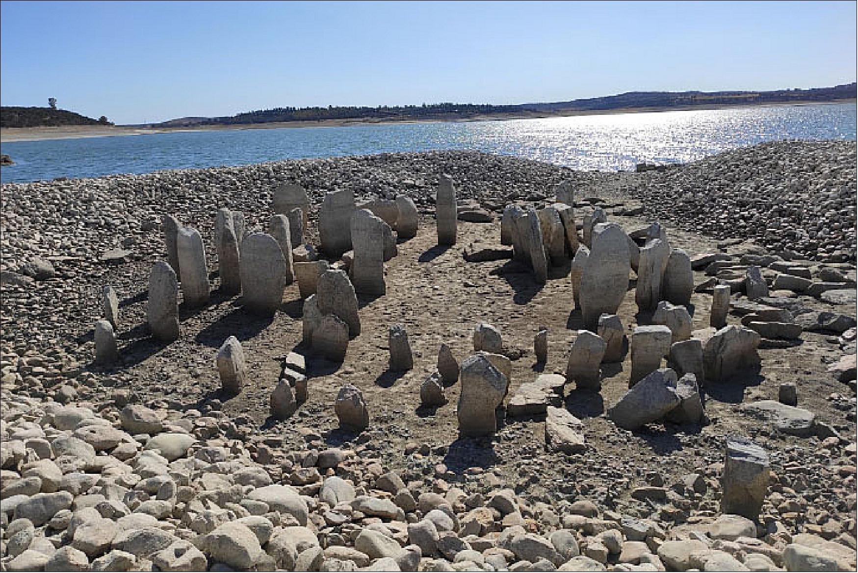 Figure 34: Since the 1960s, tips of the tallest megaliths have peaked out of the lake as water levels fluctuated. However, the dry, hot conditions in 2019 dropped lake levels to a point where the entire structure for the first time since the reservoir was filled. This photo shows the remains of the standing stones on the Dolmen of Guadalperal on 28 July 2019 (image credit: NASA Earth Observatory, photo used under the Creative Commons Attribution-Share Alike 4.0 International license, courtesy of Pleonr. Story by Kasha Patel)