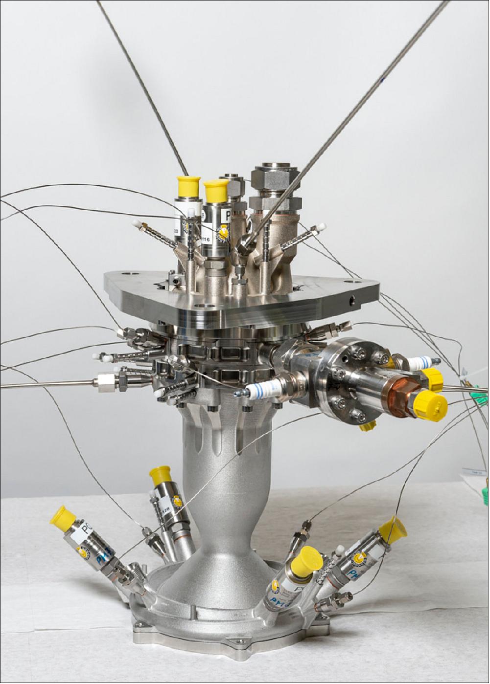 Figure 103: Developed by ArianeGroup within ESA’s Future Launchers Preparatory Program, this small-scale combustion chamber demonstrator helps to investigate flow and heat transfer phenomena on surfaces created by 3D printing – otherwise known as additive layer manufacturing. The photograph shows the combustion chamber and injector head, with the adapter rings for the DLR testing facility between them and a mounting plate. To the front, right is the igniter (image credit: ArianeGroup Holding, Jürgen Dannenberg)