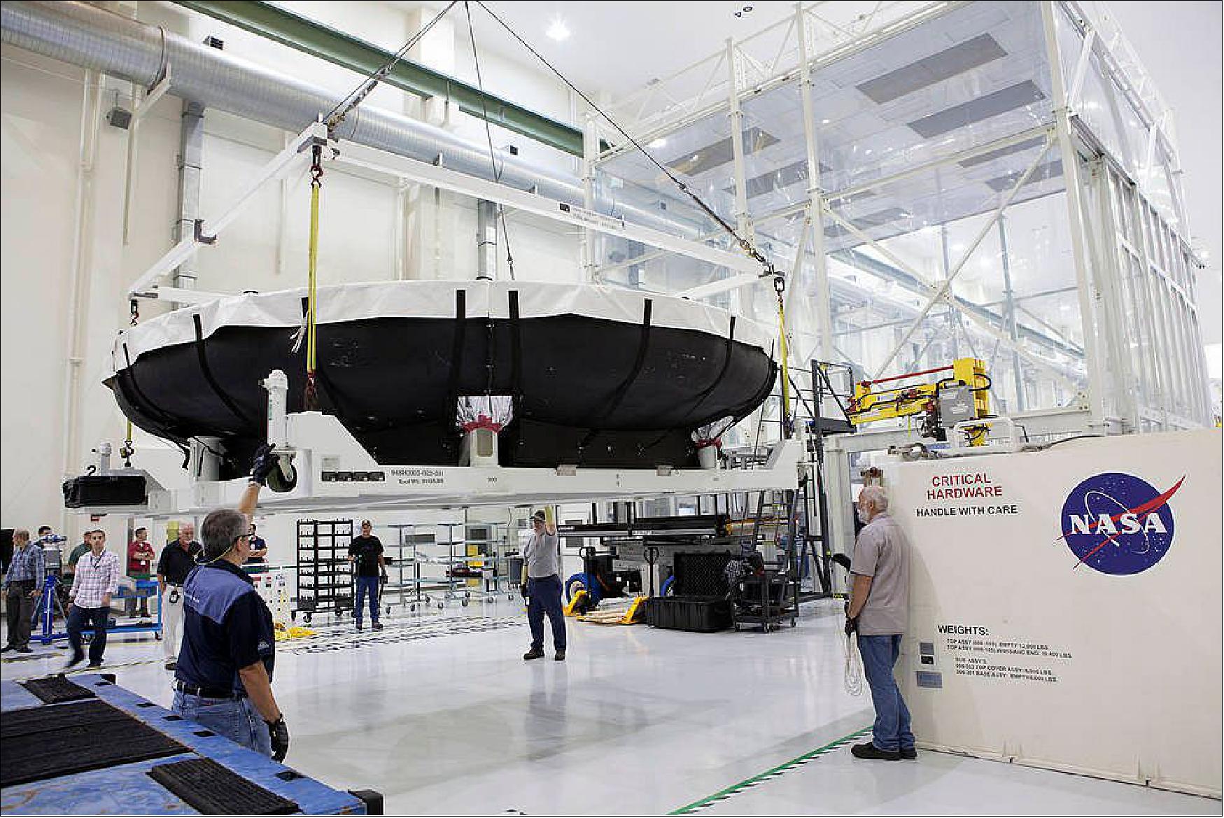 Figure 74: Inside the Neil Armstrong Operations and Checkout Building high bay at NASA’s Kennedy Space Center in Florida, technicians assist as a crane lifts the Orion heat shield for EM-1 away from the base of its shipping container (image credit: NASA, Dimitri Gerondidakis)