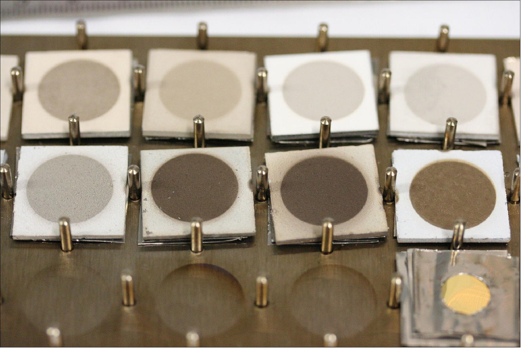 Figure 122: BepiColombo material samples after testing: Sample degradation after BepiColombo lifetime testing for ceramic reflective-surface thermal control materials. Only the central circle of each sample is exposed during testing, the border of each square revealing the original hue. Testing took place at 450ºC with UV radiation equivalent 10 times the sun for 25,000 hours under high vacuum conditions. The smaller the difference between the center and the edge, the more successful the test (image credit: ESA)