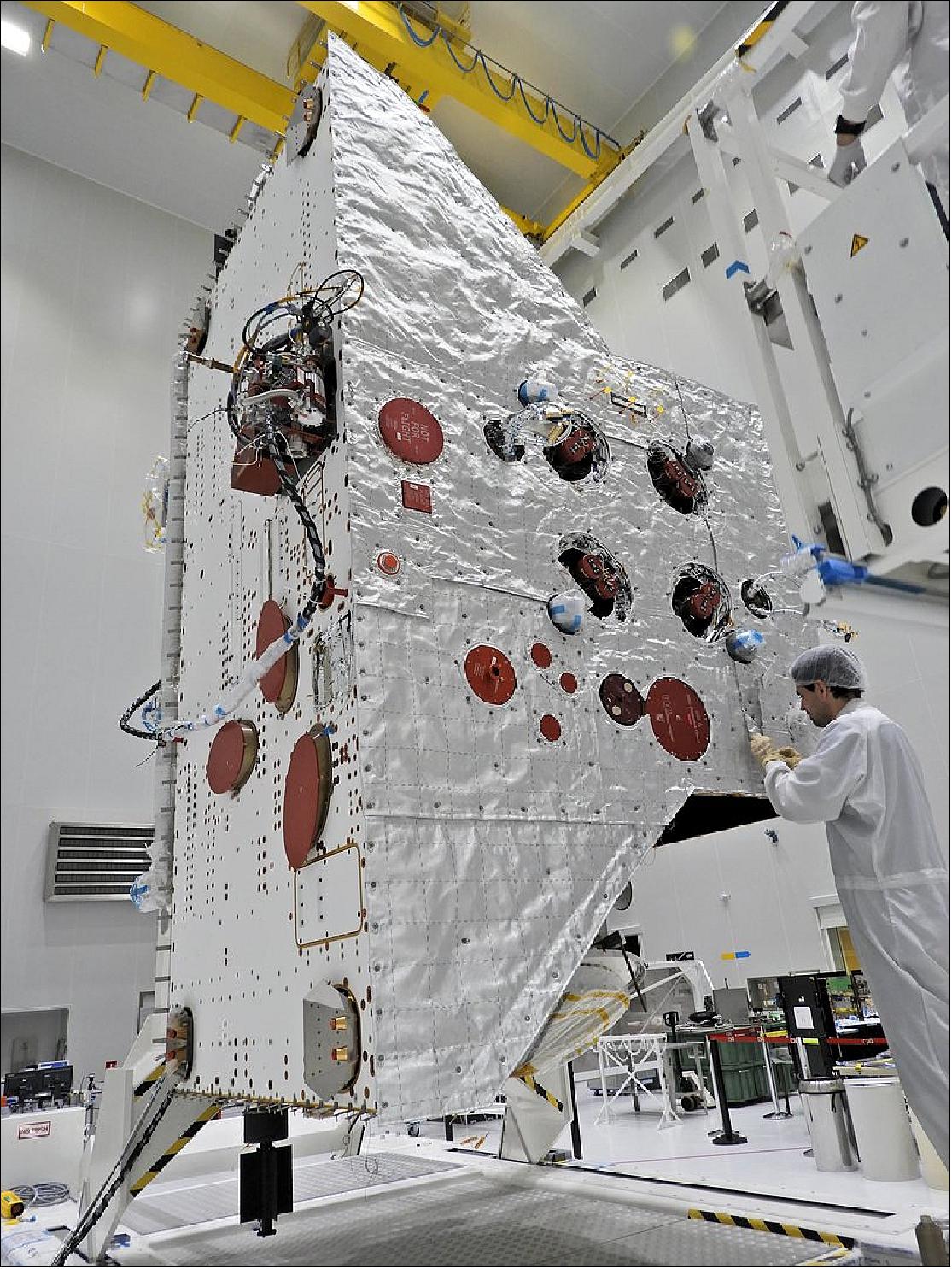 Figure 119: One of the main activities in recent weeks for the BepiColombo team at Europe’s Spaceport in Kourou has been the installation of multi-layered insulation foils and sewing of high-temperature blankets on the Mercury Planetary Orbiter. The insulation is to protect the spacecraft from the extreme thermal conditions that will be experienced in Mercury orbit. While conventional multi-layered insulation appears gold-colored, the upper layer of the module’s striking white high-temperature blanket provides the focus of this image. The white blankets are made from quartz fibres. Because the fabric is not electrically conductive, to control the build-up of electrostatic charge on the surface of the spacecraft, conducting threads have been woven through the outer layer every 10 cm. The edges of the outer blanket are hand-sewn together once installed on the module, as seen in this image. - The face of the spacecraft the engineer is working on is the panel that will always look at Mercury’s surface and as such many of the science instruments are focused here. This includes the orbiter’s cameras and spectrometers, a laser altimeter and particle analyzer. The panel also has fixtures to connect the module to the Transfer Module during the cruise to Mercury. - The face of the spacecraft pointing to the left in this orientation is the spacecraft radiator, which will eventually be fitted with ‘fins’ designed to reflect heat directionally, allowing the spacecraft to fly at low altitude over the hot surface of the planet. Heat generated by spacecraft subsystems and payload components, as well as heat that comes from the Sun and Mercury and ‘leaks’ through the blankets into the spacecraft, will be conducted to the radiator by heat pipes and ultimately radiated into space. - The oval shapes correlate to star trackers, used for navigation, while a spectrometer is connected with ground support equipment towards the top. At the back of this face, the magnetometer boom can be seen folded against the spacecraft – it has now also been fitted with multi-layered insulation.