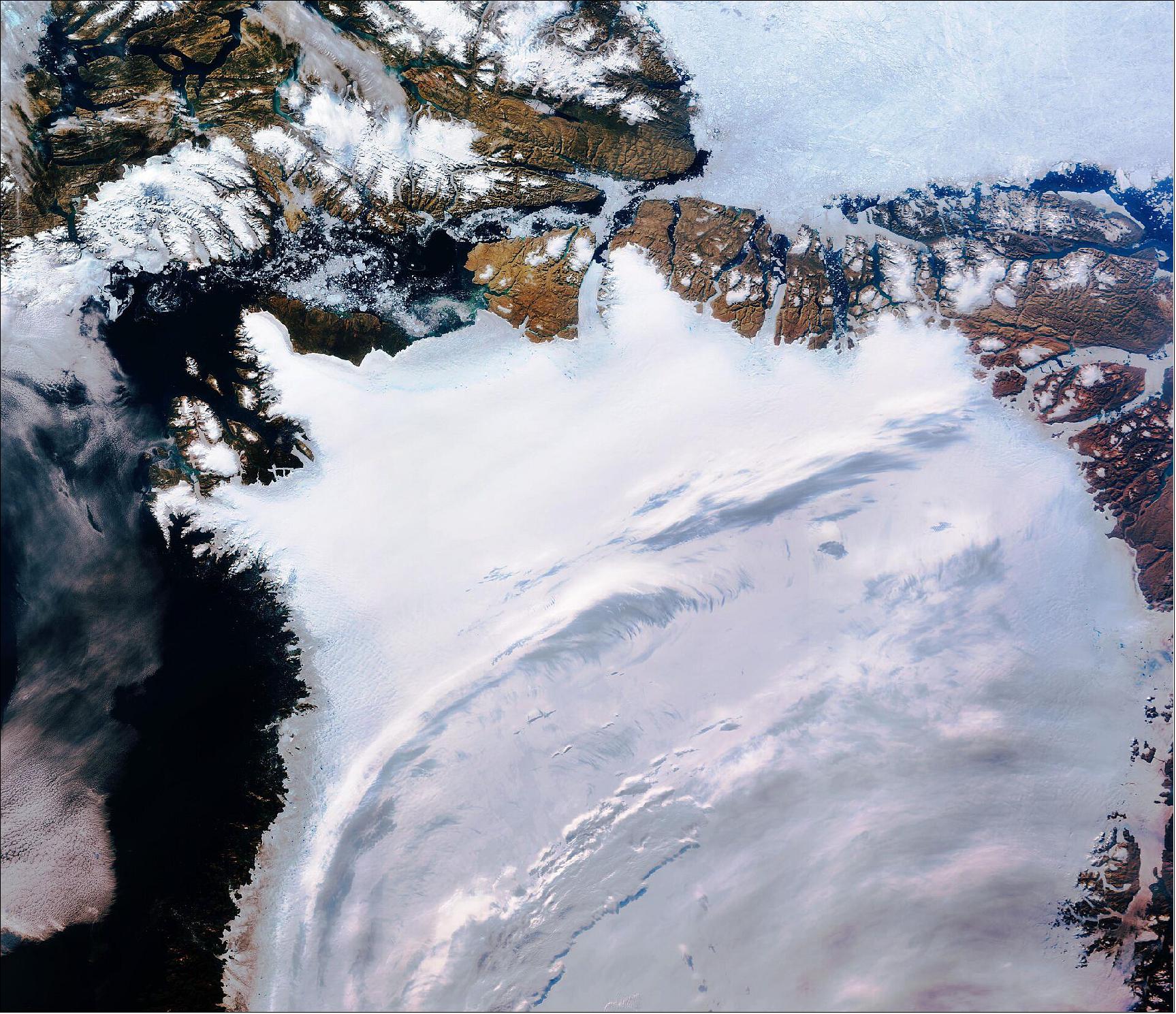 Figure 54: Northwest Greenland is featured in this icy image captured by the Copernicus Sentinel-3 mission. In the top center of this image, captured on 29 July 2019, the Petermann glacier is visible. Petermann is one of the largest glaciers connecting the Greenland ice sheet with the Arctic Ocean. Upon reaching the sea, a number of these large outlet glaciers extend into the water with a floating ‘ice tongue’. Icebergs occasionally break or ‘calve’ off these tongues. This image is also featured on the Earth from Space video program (image credit: ESA, the image contains modified Copernicus Sentinel data (2019), processed by ESA, CC BY-SA 3.0 IGO)