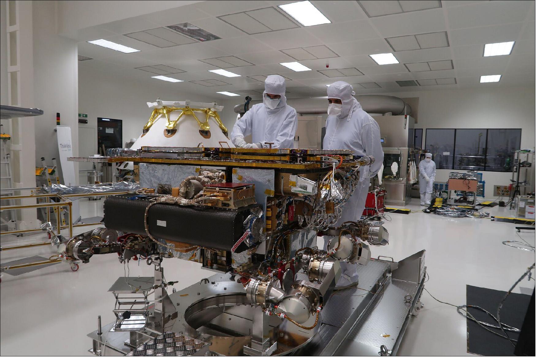 Figure 41: Workers remained fully shrouded within ‘bunny suits’ to control any kind of contamination during the packing of the ExoMars elements before shipment. In this image, two engineers work on ESA’s Rosalind Franklin rover with its solar panels and drill folded. The white capsule with golden legs in the background corresponds to the carrier module integrated with the Russian surface platform, dubbed Kazachok. These two elements will reunite with the rover in Cannes at the end of October (image credit: Thales Alenia Space)