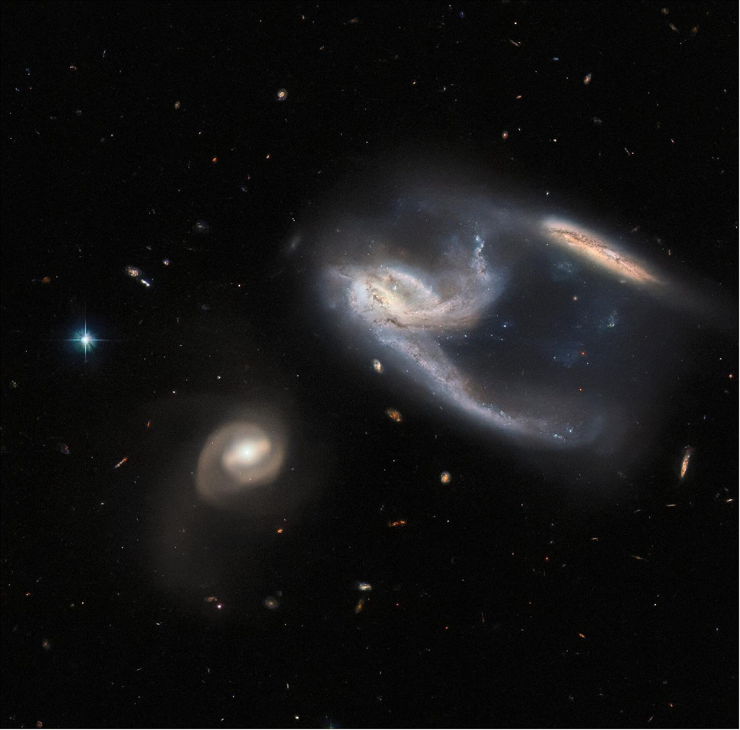 Figure 77: The subject of this image is a group of three galaxies, collectively known as NGC 7764A. They were imaged by the NASA/ESA Hubble Space Telescope, using both its Advanced Camera for Surveys (ACS) and Wide Field Camera 3 (WFC3). The two galaxies in the upper right of the image appear to be interacting with one another — indeed, the long trails of stars and gas extending from them both give the impression that they have both just been struck at great speed, thrown into disarray by the bowling-ball-shaped galaxy to the lower left of the image. In reality, however, interactions between galaxies happen over very long time periods, and galaxies rarely collide head-on with one another. It is also unclear whether the galaxy to the lower left is actually interacting with the other two, although they are so relatively close in space that it seems possible that they are. By happy coincidence, the collective interaction between these galaxies have caused the two on the upper right to form a shape, which from our Solar System's perspective, ressembles the starship known as the USS Enterprise from Star Trek! (image credit: ESA/Hubble & NASA, J. Dalcanton, Dark Energy Survey, DOE, FNAL, DECam, CTIO, NOIRLab/NSF/AURA, ESO; CC BY 4.0 Acknowledgement: J. Schmidt)
