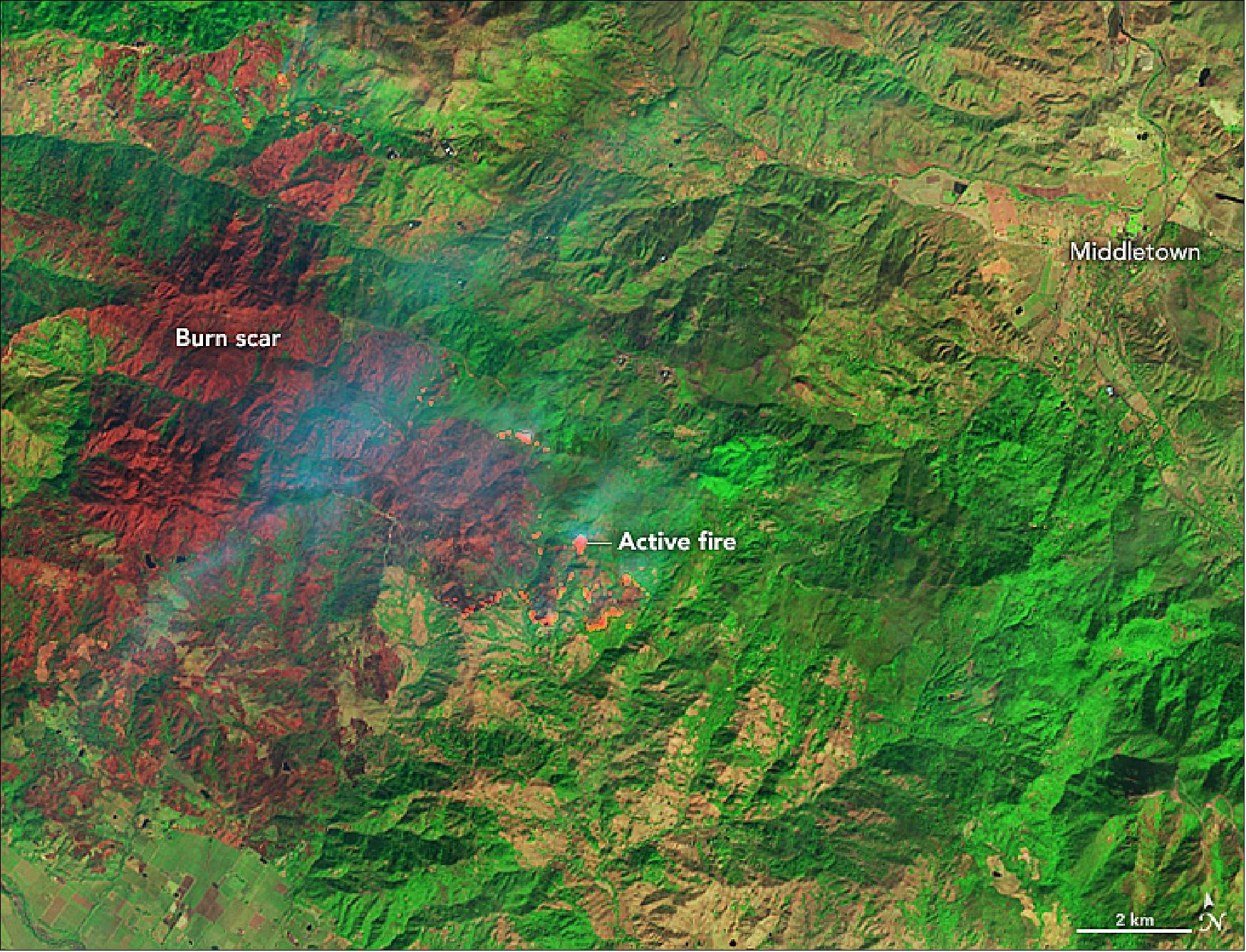 Figure 24: This image shows a false-color view of the burn scar from the Kincade Fire as it appeared on October 26, 2019. The image combines shortwave-infrared, near-infrared, and green light from Landsat 8 (OLI bands 7-5-4) to better distinguish between burned vegetation (brown) and unburned vegetation (green). The brightest reds are active fire fronts. - The Kincade fire fits with a trend of larger, more destructive fires in California in autumn; fires in this season are strongly influenced by winds and dry weather. In addition to the impending wind storm, dry weather is expected continue in Northern California for the remainder of the week (image credit: NASA Earth Observatory, image by Joshua Stevens and Lauren Dauphin, using Landsat data from the U.S. Geological Survey and GEOS-5 data from the Global Modeling and Assimilation Office at NASA GSFC. Story by Kasha Patel)