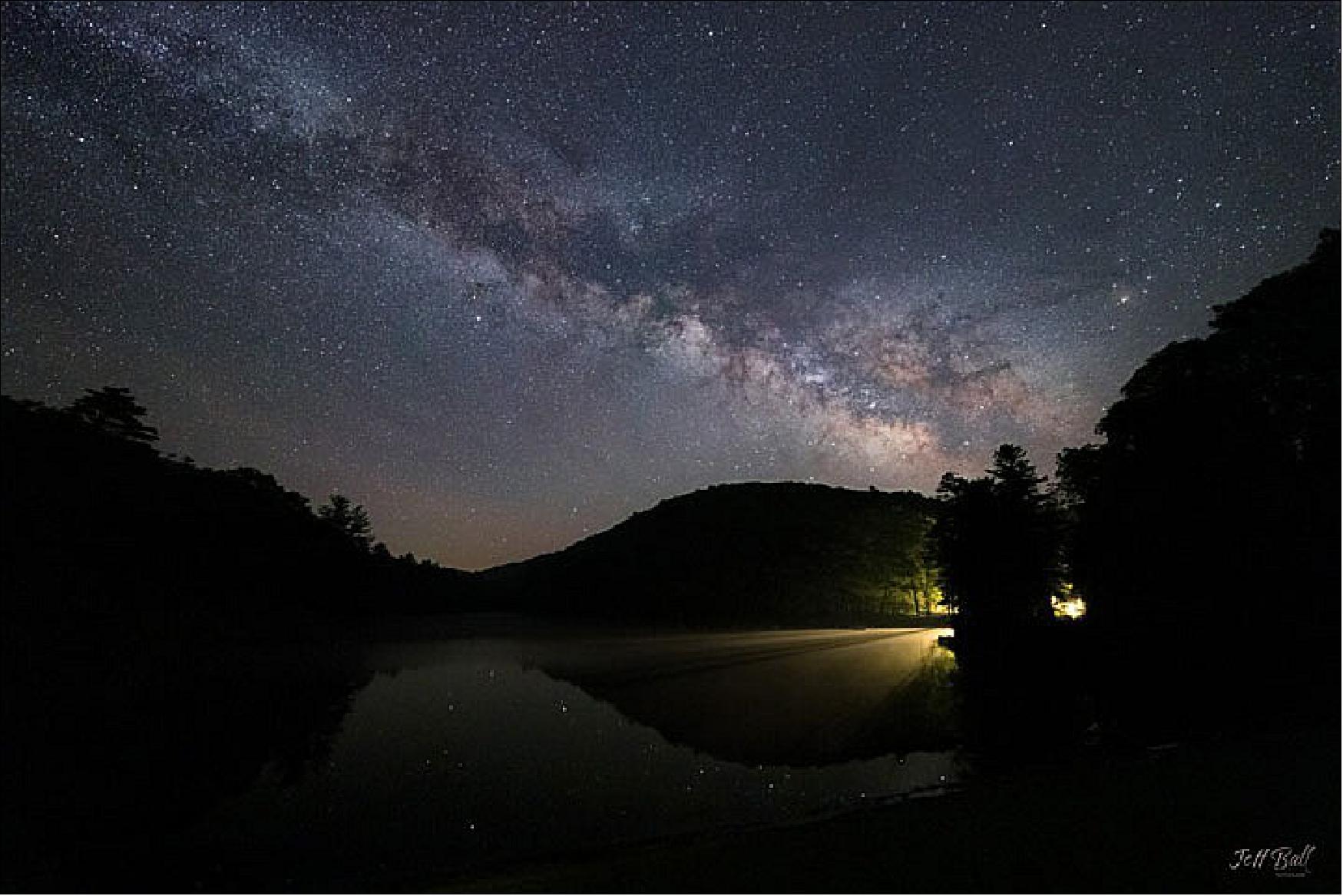 Figure 35: Even designated dark sky parks are not completely dark. Instead, they are lit by natural sources such as starlight and moonlight. The celestial light show draws amateur astronomers, stargazers, and photographers. The photograph below, shot by Jeff Ball, shows the Milky Way over Watoga Lake. The name Watoga is the Cherokee word for “starry waters,” according to the park’s website (image credit: NASA Earth Observatory)