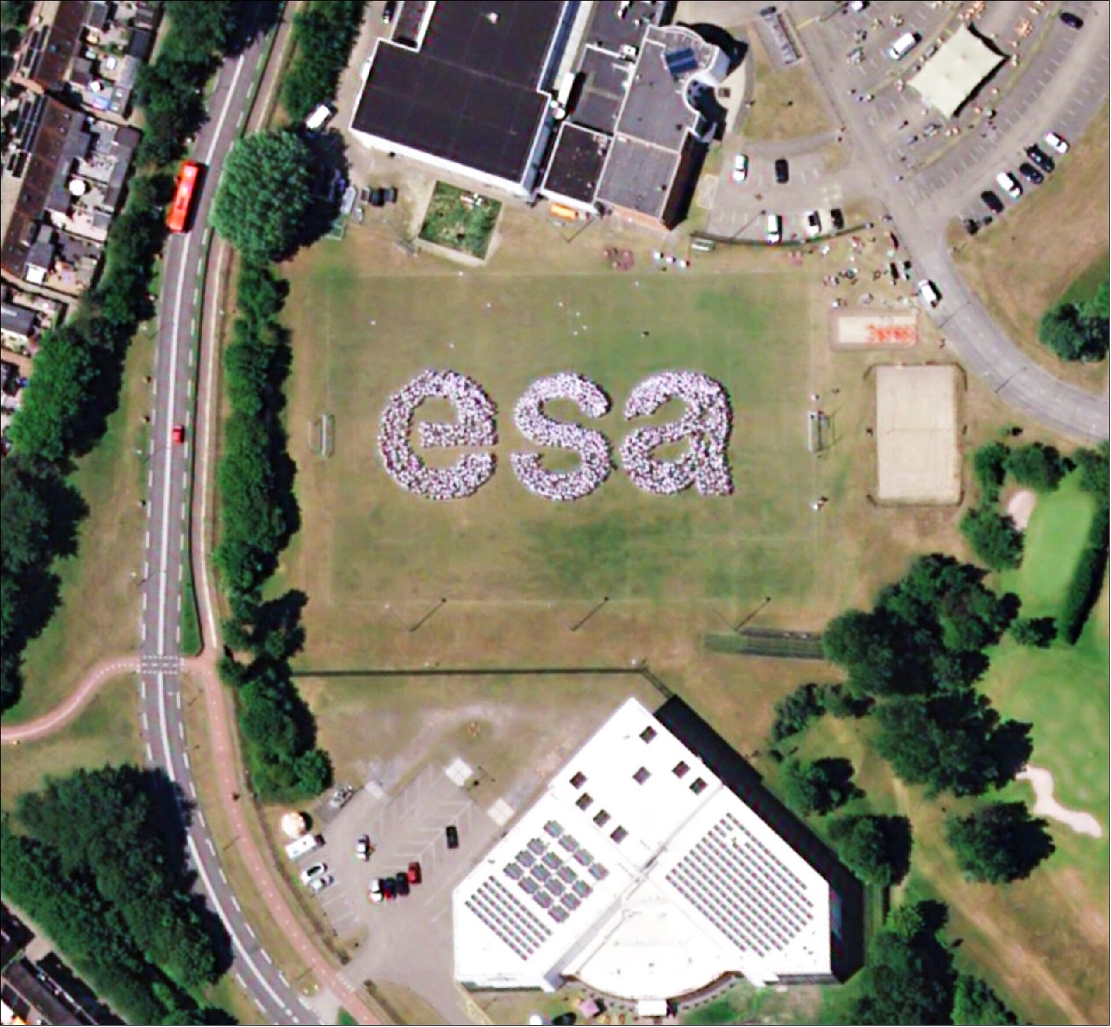 Figure 11: People gathered on ESTEC’s rugby field in the run-up to the satellite pass, holding white sheets of paper over their heads to make them stand out against the green grass around them (image credit: ESA)