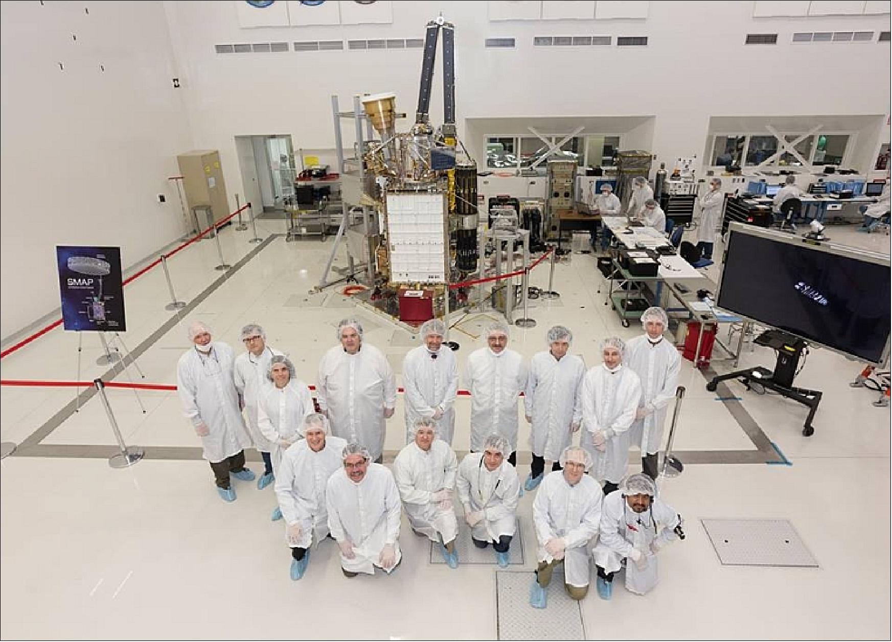 Figure 8: Photo of the SMAP leadership and test team members in cleanroom garb appear with the Spacecraft and Instrument in the background (image credit: NASA)