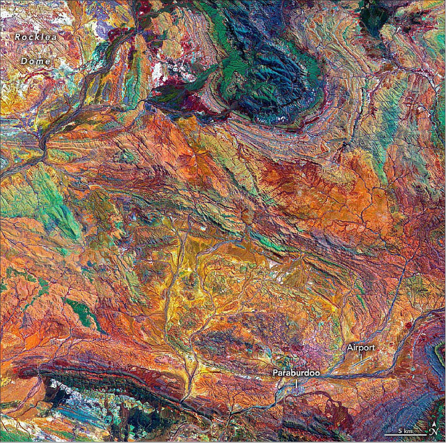 Figure 21: The image was acquired by the Advanced Spaceborne Thermal Emission and Reflection Radiometer (ASTER) on NASA’s Terra satellite on October 12, 2004. It is a composite of ASTER bands 4-2-1. These bands detect shortwave-infrared light, near-infrared and visible red light, and green light, which are displayed as red, green, and blue, respectively. In this display, iron-rich rocks appear yellow to green. Light-colored, iron-poor rocks appear white, while dark-colored iron-poor rocks are dark blue. Areas with more vegetation cover appear dark red. This is because plants reflect more near-infrared than green light. A linear contrast stretch has also been applied to the image to enhance the color contrast and help distinguish rock types (image credit: NASA Earth Observatory image by Joshua Stevens, using data from NASA/METI/AIST/Japan Space Systems, and the U.S./Japan ASTER Science Team. Story by Sara E. Pratt)